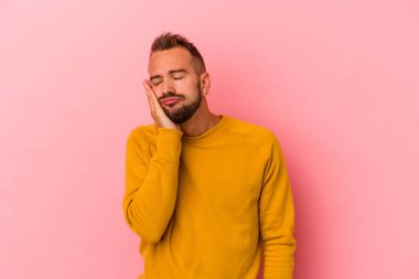 Pembe arka planda dövmeleri olan, sıkılmış, yorgun ve dinlenmeye ihtiyacı olan beyaz, genç bir adam..