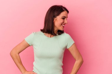 Pembe arka planda izole edilmiş genç beyaz kadın gülüyor ve gözlerini kapıyor, rahatlamış ve mutlu hissediyor..