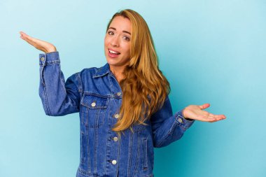 Mavi arka planda izole edilmiş beyaz bir kadın. Kafası karışmış ve omuz silkiyor. Kopya alanını tutmak için..