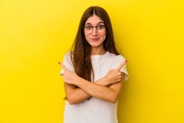 Sarı arka plan noktalarında izole edilmiş genç beyaz kadın iki seçenek arasında seçim yapmaya çalışıyor..