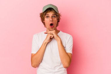 Makyajlı beyaz bir adam pembe arka planda izole edilmiş şans için dua ediyor, şaşırmış ve ağzını açıyor..