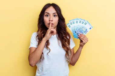 Sarı arka planda izole edilmiş banknotlar tutan genç melez kadın ya sır saklıyor ya da sessizlik istiyor..