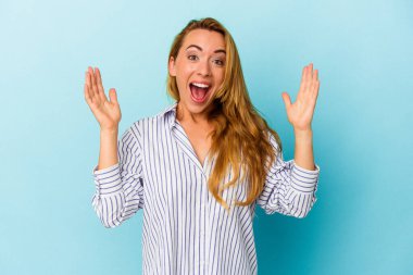 Mavi arka planda izole edilmiş beyaz kadın zaferi ya da başarıyı kutluyor, şaşırıyor ve şok oluyor..