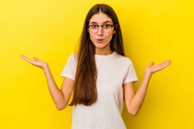 Sarı arka planda izole edilmiş genç, beyaz bir kadın. Kafası karışmış ve omuz silkiyor. Kopya alanını tutmak için..