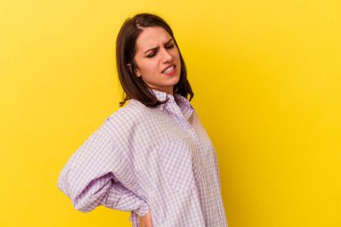 Sarı arka planda izole edilmiş beyaz bir kadın sırt ağrısı çekiyor..