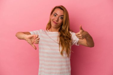 Beyaz tenli sarışın kadın pembe arka planda izole edilmiş. Baş parmağını kaldırıyor ve baş parmağını aşağı gösteriyor. Zor seçim konsepti.