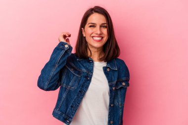 Pembe arka planda izole edilmiş genç beyaz kadın bir şeye gülüyor, elleriyle ağzını kapatıyor..