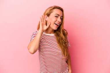 Kafkasyalı sarışın kadın pembe arka planda izole edilmiş bir şekilde bir dedikoduyu dinlemeye çalışıyor..