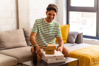 Genç melez adam pizza yiyor, burger yiyor ve bira içiyor.