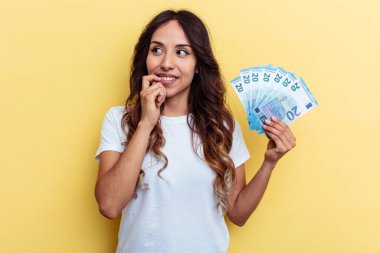 Sarı arka planda izole edilmiş banknotları tutan genç bir ırk kadını rahat bir şekilde fotokopi odasına bakan bir şeyi düşünüyor..