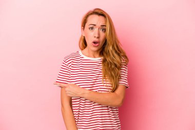 Pembe arka planda izole edilmiş beyaz sarışın kadın yan tarafı işaret ediyor.