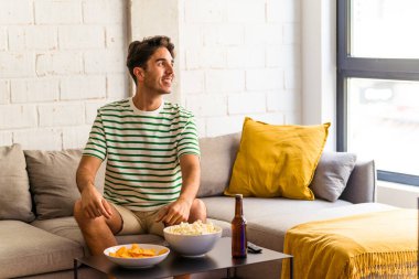 Genç melez adam kanepede oturmuş patlamış mısır yiyor. Gülümsüyor, neşeli ve keyifli..