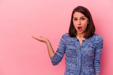 Pembe arka planda izole edilmiş genç beyaz kadın, avuç içi fotokopi alanını elinde tutmaktan etkilenmiş..