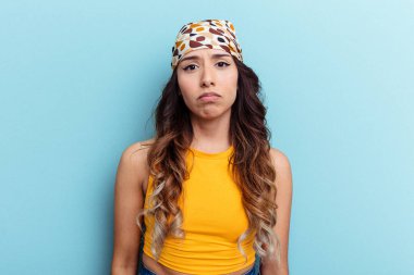 Mavi arka planda izole edilmiş genç Meksikalı kadın yanakları patlatıyor, yorgun bir ifadesi var. Yüz ifadesi kavramı.