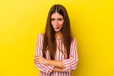 Sarı arka planda izole edilmiş, hoşnutsuzca kaşlarını çatmış, kollarını kavuşturmuş genç beyaz bir kadın..