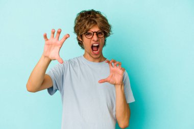 Mavi arka planda, pençelerini kedi taklidi yaparken gösteren, makyajlı genç beyaz bir adam. Saldırgan bir hareket..