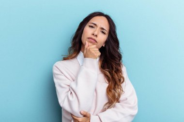 Mavi arka planda izole edilmiş genç Meksikalı kadın şüpheli, belirsiz, seni muayene ediyor..