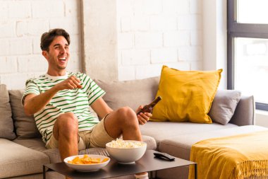 Genç melez adam kanepede oturmuş patlamış mısır yiyor.