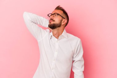 Dövmeleri olan beyaz bir genç adam pembe arka planda izole edilmiş dirsek masajı yapıyor, kötü bir hareketin ardından acı çekiyor..