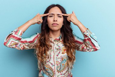 Mavi arka planda izole edilmiş genç Meksikalı kadın bir işe odaklanmış, işaret parmaklarını işaret ediyor..