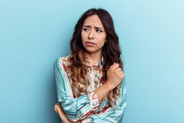 Mavi arka planda izole edilmiş genç Meksikalı kadın kafası karışmış, şüpheli ve güvensiz hissediyor..
