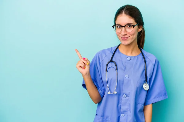 Jonge Blanke Verpleegster Geïsoleerd Blauwe Achtergrond Lachend Terzijde Wijzend Iets — Stockfoto