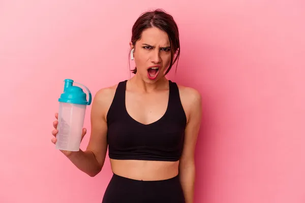 若いですCaucasian女性飲むタンパク質シェイク隔離されたピンクの背景悲鳴非常に怒っていると積極的 — ストック写真