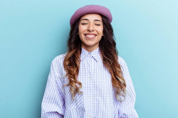 Young mexican woman isolated on blue background laughs and closes eyes, feels relaxed and happy.