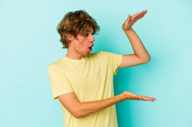 Mavi arka planda izole edilmiş beyaz makyajlı genç bir adam elleri arasında bir fotokopi alanı tutarken şok ve hayrete düştü..