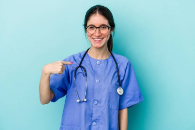 Kafkasyalı genç hemşire mavi arka planda izole edilmiş. Elle bir tişört fotokopi alanını gösteriyor. Gururlu ve kendinden emin.