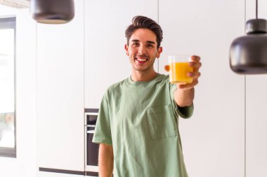 Genç melez adam mutfağında portakal suyu içiyor.