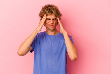 Makyajlı beyaz bir adam pembe arka planda izole edilmiş, başı ağrıyor, yüzüne dokunuyor..