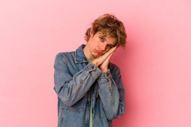 Pembe arka planda soyutlanmış beyaz makyajlı genç bir adam esneyerek ağzını eliyle kapatan yorgun bir jest yapıyor..