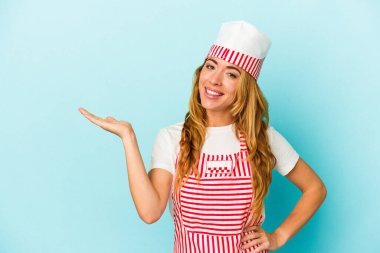 Caucasian ice cream maker woman isolated on blue background  showing a copy space on a palm and holding another hand on waist. clipart