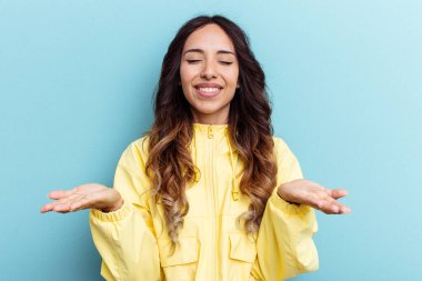 Mavi arka planda izole edilmiş genç Meksikalı kadın elinde avuç içi bir şeyle kameraya sunuyor..