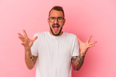 Pembe arka planda izole edilmiş dövmeleri olan genç beyaz bir adam gökyüzüne haykırıyor, yukarı bakıyor ve hayal kırıklığına uğruyor..