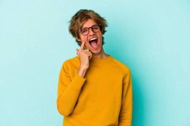 Makyajlı beyaz bir adam mavi arka planda izole edilmiş ağlıyordu, bir şeyden mutsuzdu, ıstırap ve kafa karışıklığı içeriyordu..