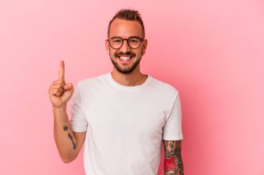 Pembe arka planda dövmeleri olan beyaz genç bir adam bir numarayı parmağıyla gösteriyor..