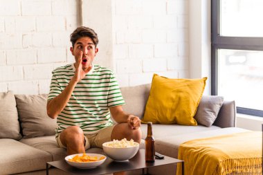 Kanepede oturmuş patlamış mısır yiyen genç ırk gizli bir sıcak fren haberi veriyor ve yan bakıyor.