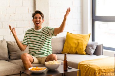 Genç melez adam kanepede oturmuş patlamış mısır yiyor. Hoş bir sürprizle karşılaşıyor. Heyecanlı ve el kaldırıyor..