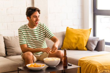 Genç melez adam kanepede oturmuş patlamış mısır yiyor.