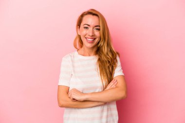 Pembe arka planda kendini güvende hisseden, kararlılıkla kollarını kavuşturan beyaz sarışın kadın..