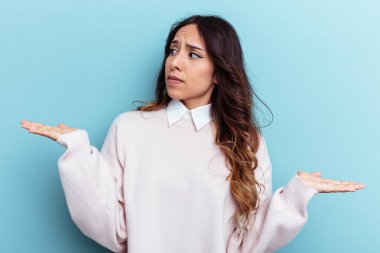 Mavi arka planda izole edilmiş genç Meksikalı kadın. Kopya alanını tutmak için kafası karışık ve omuz silkiyor..