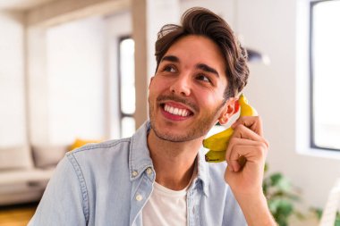 Genç melez bir adam evinin mutfağında muz yiyor.