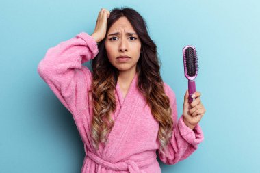 Mavi arka planda izole edilmiş bir fırça tutan bornoz giyen genç Meksikalı kadın şok olmuştu..