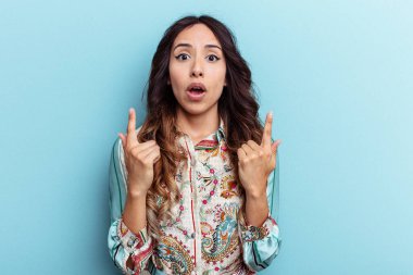 Mavi arka planda izole edilmiş genç Meksikalı kadın ağzı açık bir şekilde üst tarafı işaret ediyor..