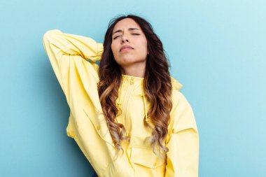 Mavi arka planda izole edilmiş genç Meksikalı kadın stresten dolayı boynu ağrıyor, masaj yapıyor ve elle dokunuyor..