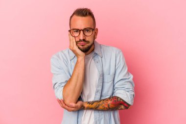 Pembe arka planda dövmeleri olan, sıkılmış, yorgun ve dinlenmeye ihtiyacı olan beyaz, genç bir adam..