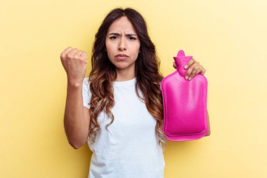 Sarı arka planda izole edilmiş sıcak bir çanta taşıyan genç bir ırk kadını kameraya yumruk gösteriyor, agresif bir yüz ifadesi..