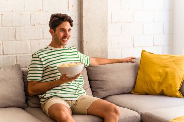 Genç melez adam kanepede oturmuş patlamış mısır yiyor.